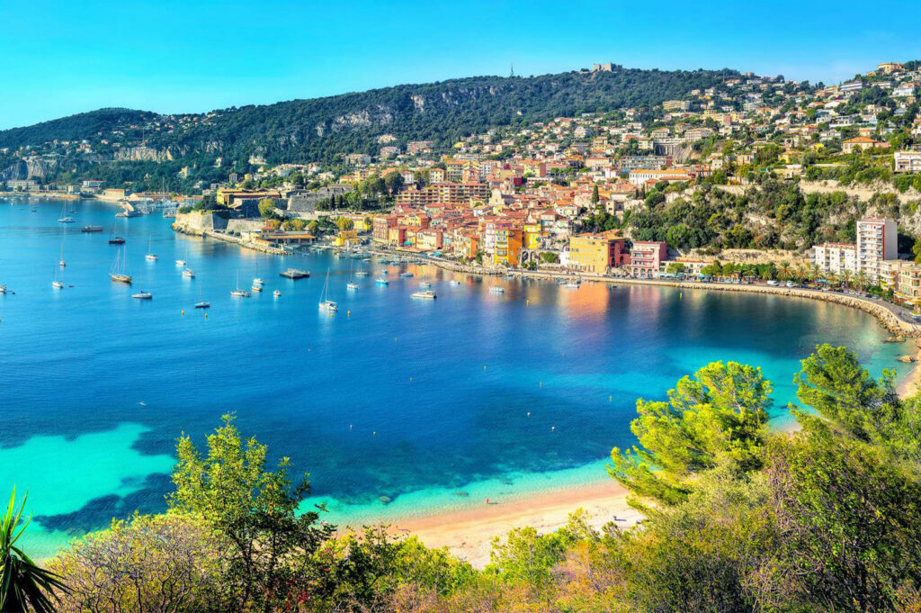 Panoramic view of the colorful seaside village of Villefranche-sur-Mer, France, nestled along the deep blue waters of the Côte d'Azur bay.