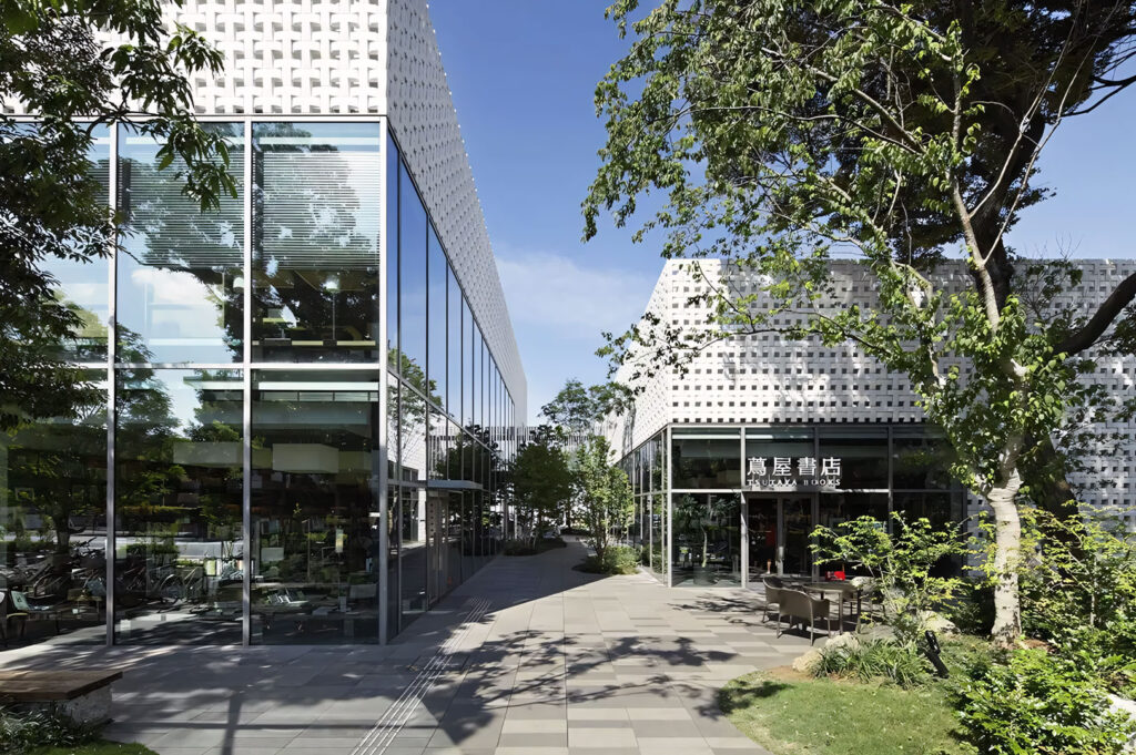 Modern Japanese architectural complex (likely Tsutaya Books/T-Site in Tokyo) featuring large glass facades and geometric white lattice screens surrounded by trees on a sunny day.