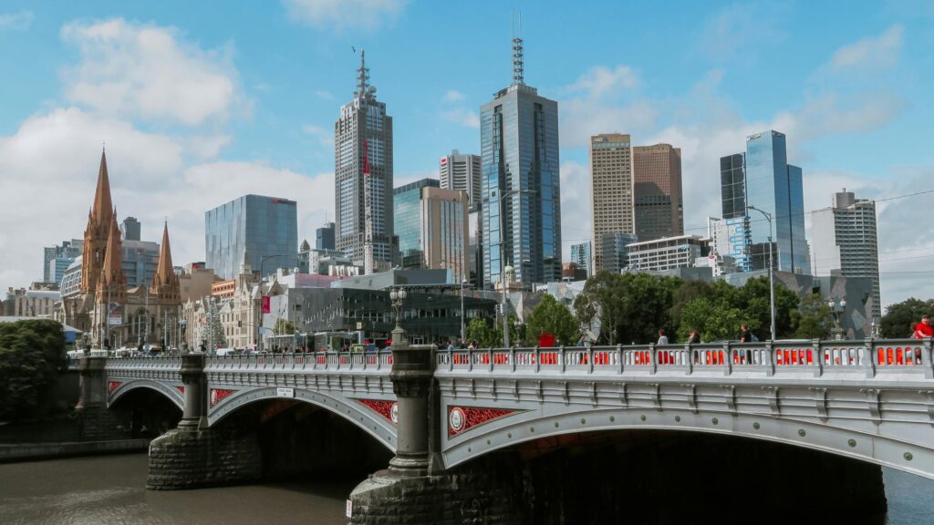 This is a wide, elevated view capturing the cityscape of Melbourne, Australia, centered around the Yarra River and the Princes Bridge in the foreground.