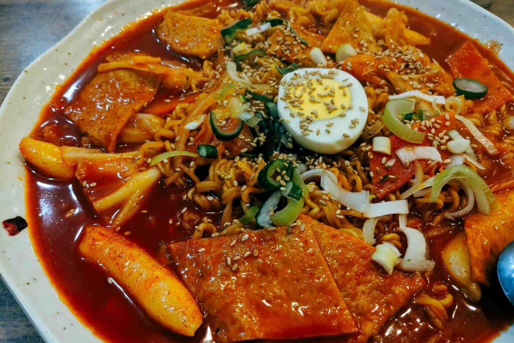 This close-up, high-angle shot features a vibrant and spicy-looking Korean dish, most likely Rabokki or Tteokbokki, served in a white dish.