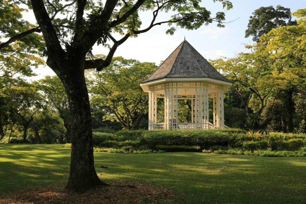 White Bandstand gazebo in Singapore Botanic Gardens surrounded by lush green trees.