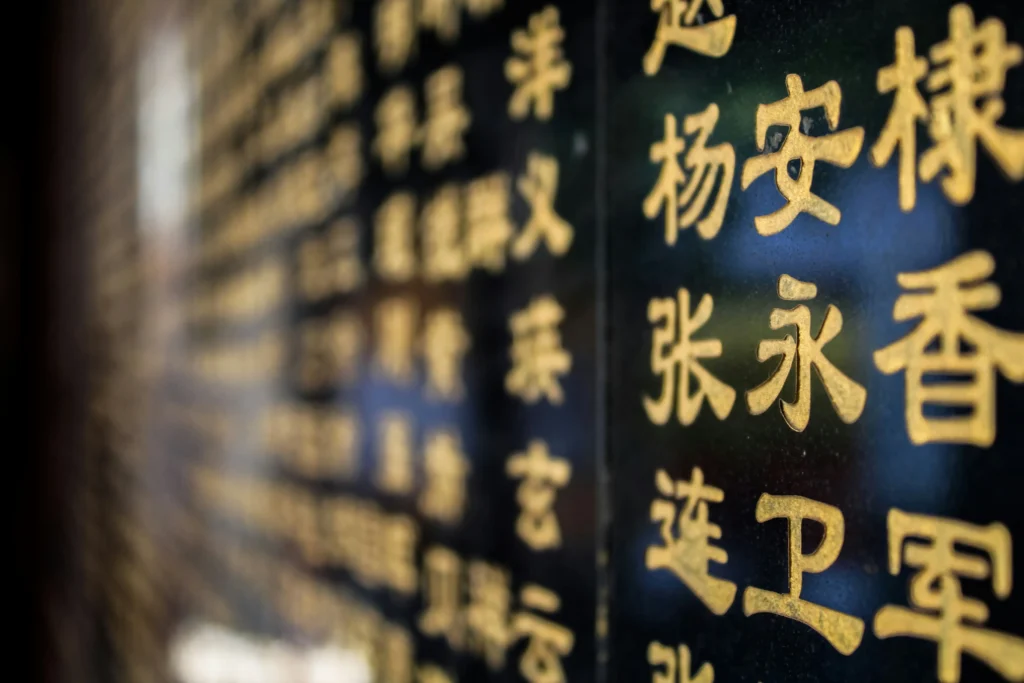 This image captures a close-up, shallow-depth-of-field shot of golden Chinese characters engraved onto a polished black stone surface. The foreground characters are sharp and legible, while the rest of the inscriptions blur into a soft, glowing bokeh effect as they recede into the distance.