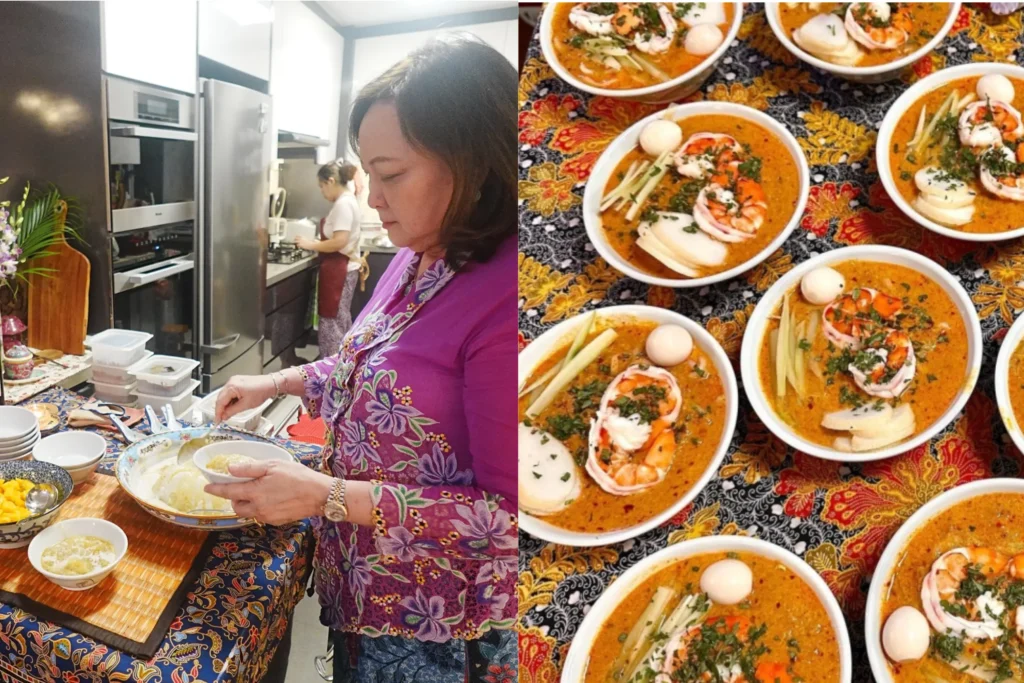 A woman in a purple and floral Peranakan kebaya prepares bowls of food on a table covered in a traditional batik cloth. On the right, multiple bowls of Laksa are neatly arranged, garnished with shrimp, hard-boiled eggs, and fresh herbs.
