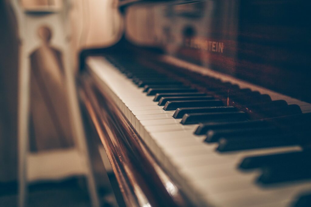 This close-up shot captures the keys of a vintage piano, featuring a shallow depth of field that keeps the mid-range keys in sharp focus while the background remains softly blurred. The warm, moody lighting emphasizes the polished wood grain and the elegant, weathered texture of the instrument.