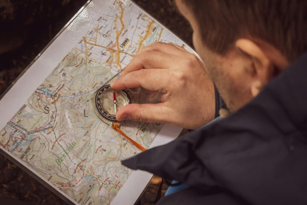 A person focuses on a detailed topographic map while carefully positioning a compass to find their way. The close-up shot emphasizes the navigator’s hand and the intricate geography of the trail ahead.