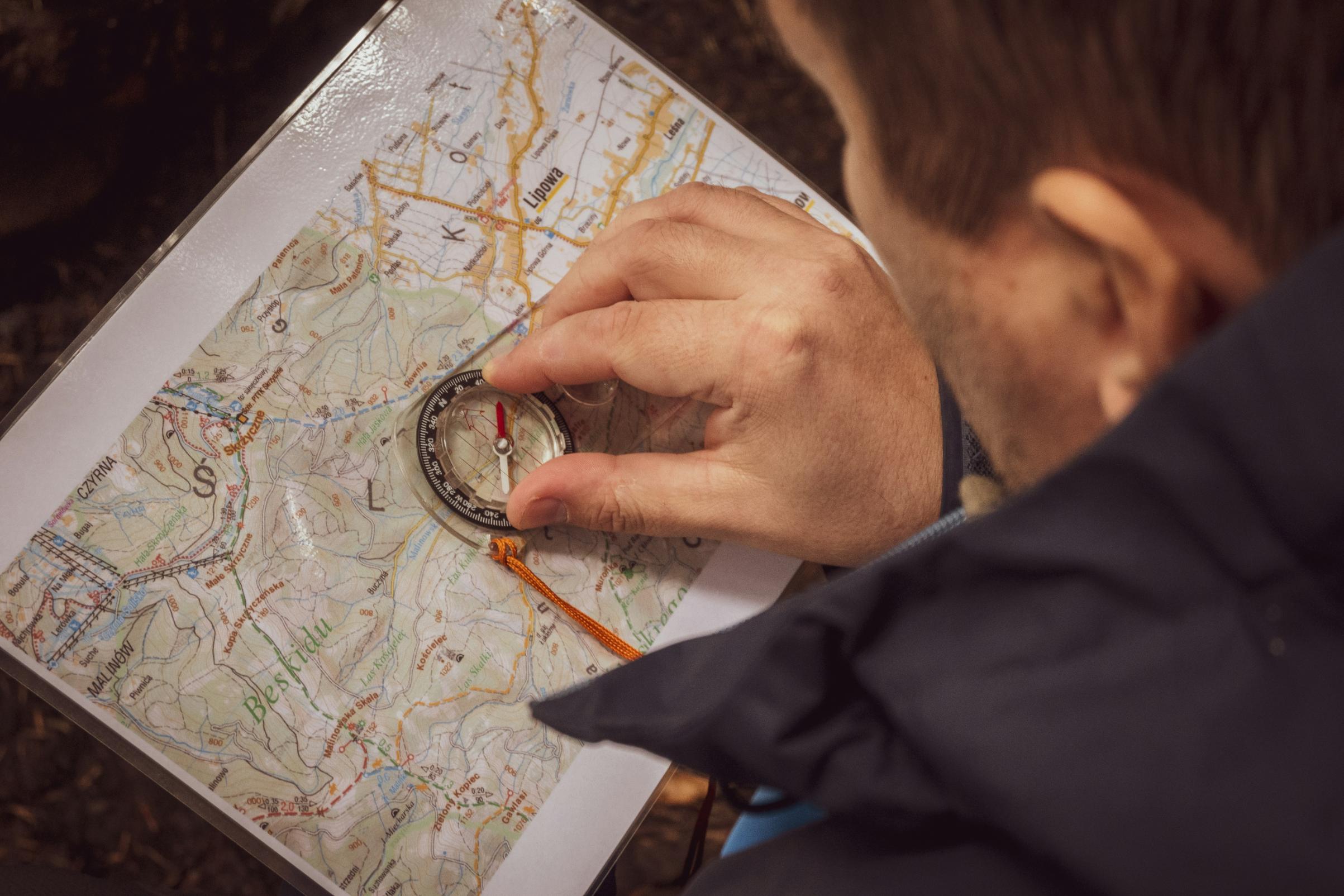 A person focuses on a detailed topographic map while carefully positioning a compass to find their way. The close-up shot emphasizes the navigator’s hand and the intricate geography of the trail ahead.