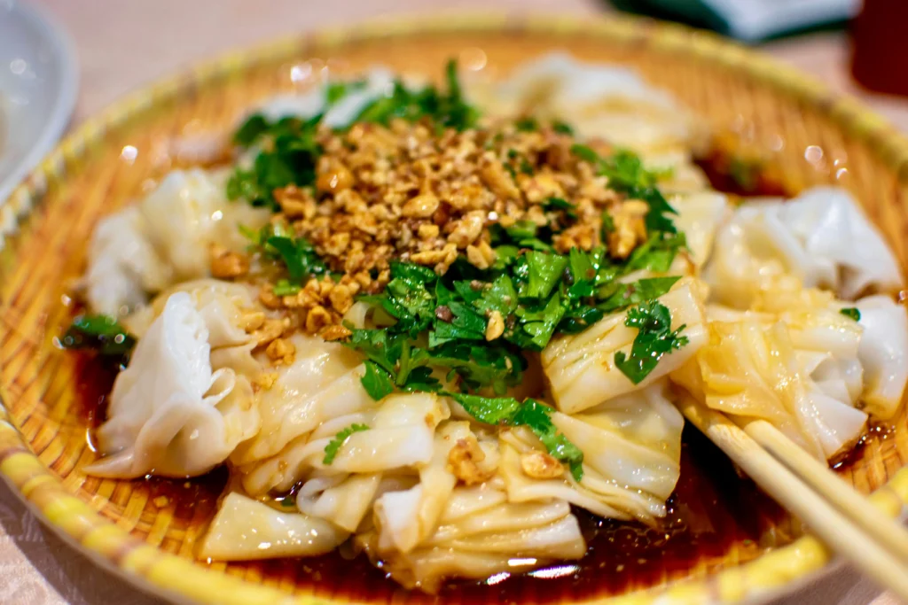 A close-up shot of a local Singaporean rice noodle dish, topped with a generous layer of chopped green herbs, cilantro, and crushed peanuts in a savory dark soy sauce.