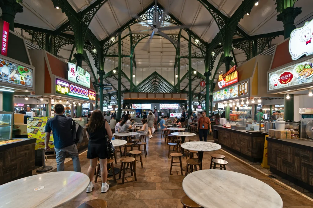 Interior view of the historic Lau Pa Sat hawker center in Singapore, showcasing its iconic green Victorian cast-iron structure, high ceilings, and bustling food stalls.