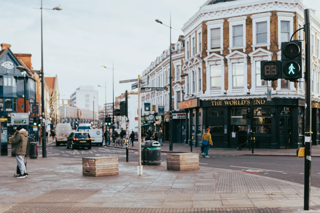 The image shows a bustling street scene in London, featuring "The World's End" pub on a prominent street corner. Pedestrians walk along the sidewalks while several vehicles navigate the intersection under an overcast sky.