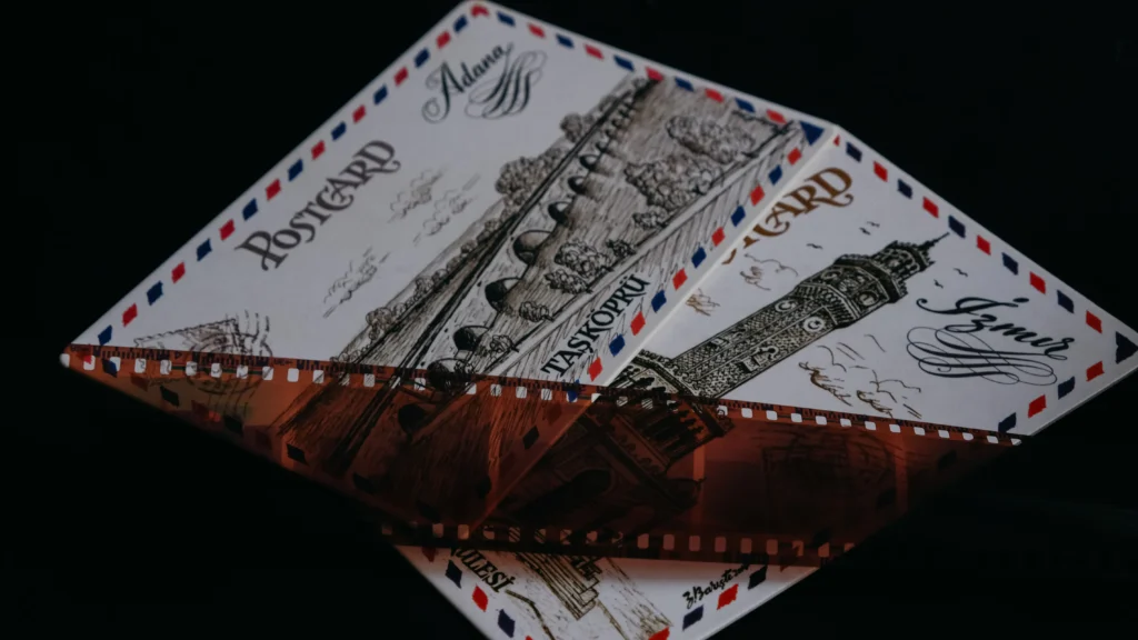 Two vintage illustrated postcards featuring Turkish landmarks and classic airmail borders rest against a dark background. A strip of translucent camera film negative lies diagonally across the cards, enhancing the nostalgic theme.