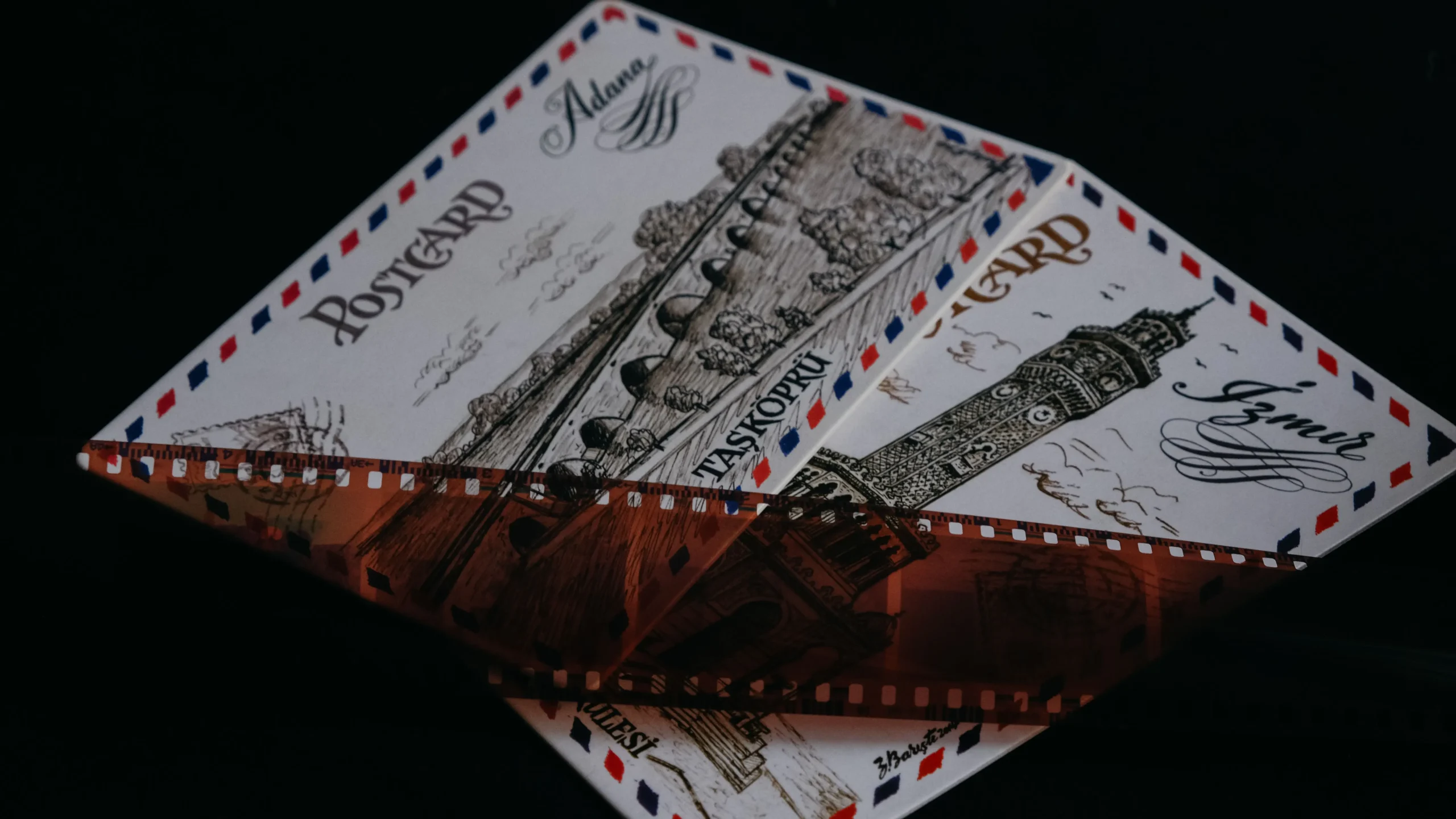 Two vintage illustrated postcards featuring Turkish landmarks and classic airmail borders rest against a dark background. A strip of translucent camera film negative lies diagonally across the cards, enhancing the nostalgic theme.