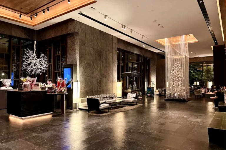 Elegant Kimpton Maa-Lai Bangkok lobby with dark wood interiors, lounge seating, warm lighting, and a decorative hanging installation.