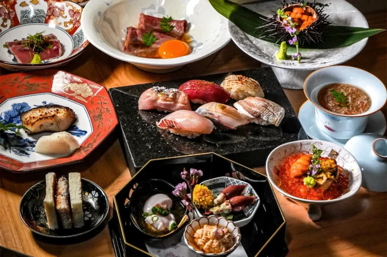 Assorted Japanese omakase dishes arranged on a wooden dining table, including sushi, sashimi, uni, soup, and small plated appetizers.