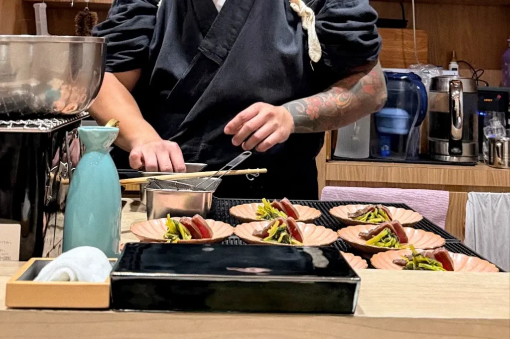 Chef preparing multiple plated omakase dishes at a Japanese restaurant counter.