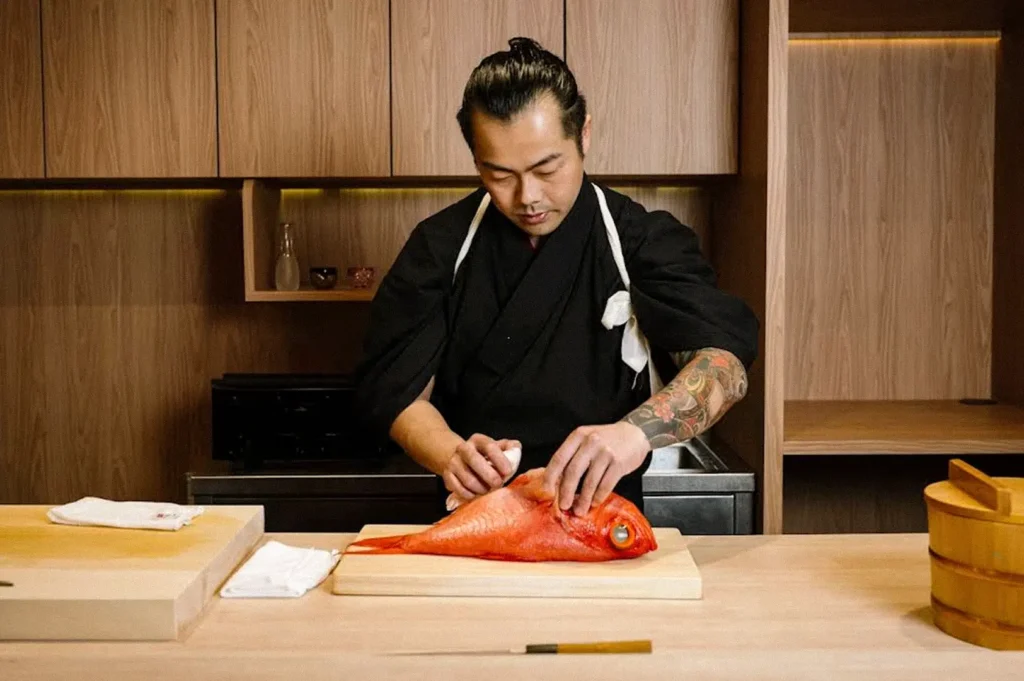 Japanese chef carefully preparing a whole fish on a cutting board at a restaurant counter.