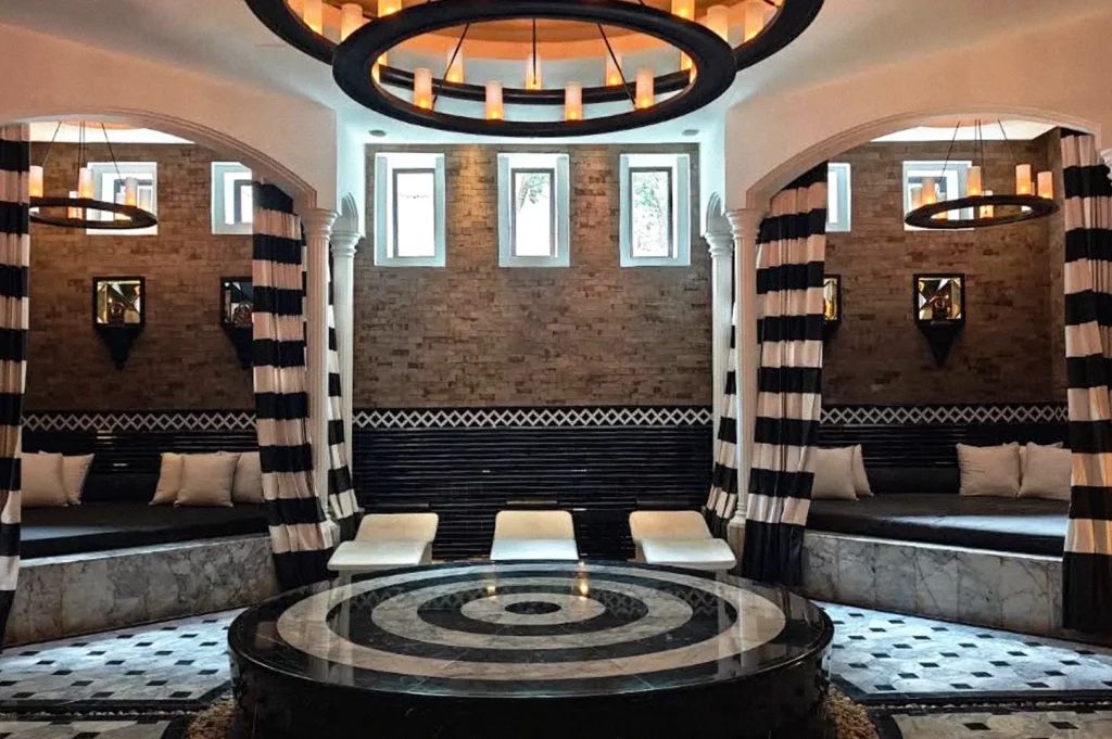 An elegant lounge with black-and-white striped curtains, curved seating, patterned floors, and large circular pendant lights surrounding a round marble table.