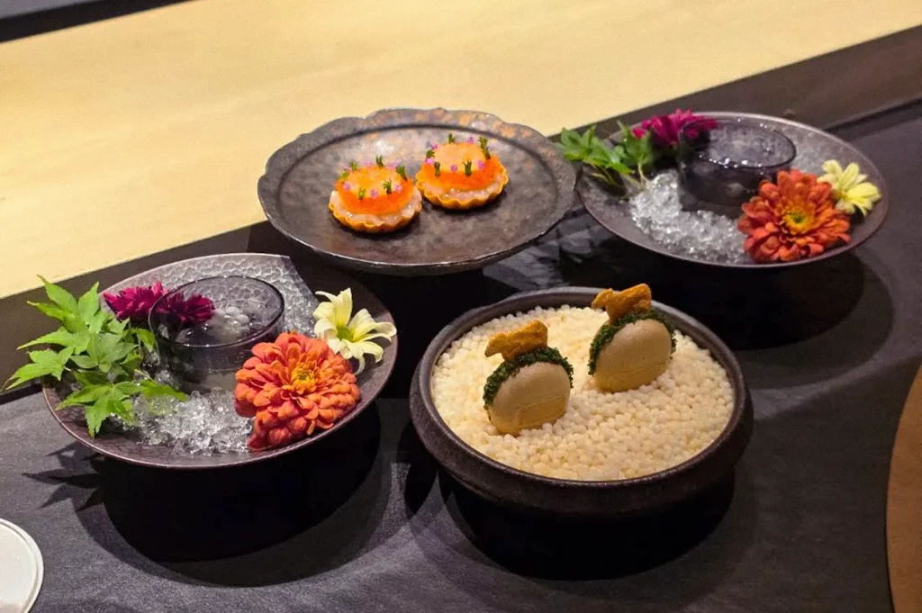 A selection of elegantly plated Japanese omakase dishes garnished with edible flowers and fresh herbs.