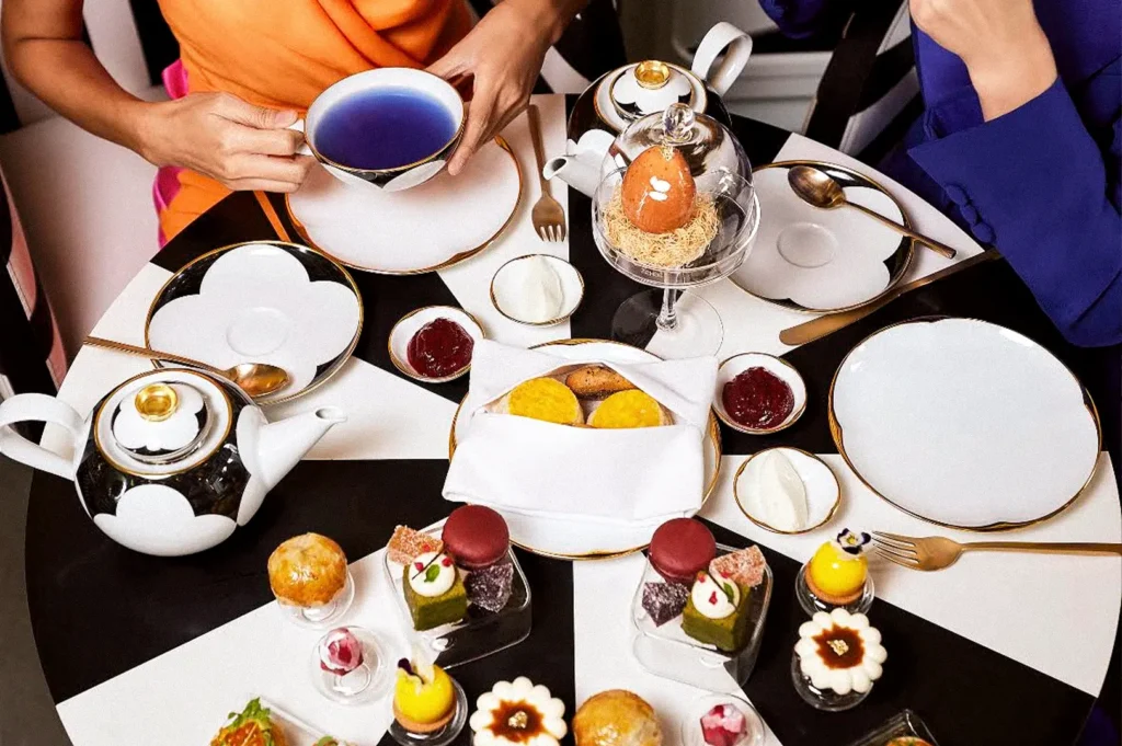 Afternoon tea served on elegant black-and-white tableware, featuring colorful pastries, cakes, scones, tea, and fruit desserts.