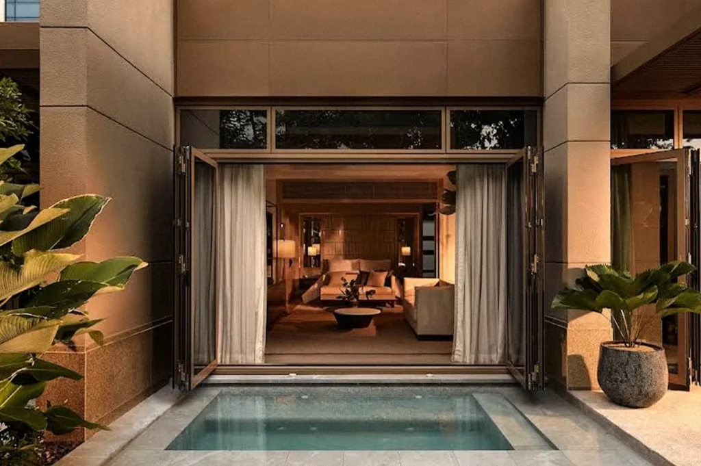 Private hotel courtyard with a small plunge pool leading into a warmly lit interior lounge, surrounded by tropical plants.