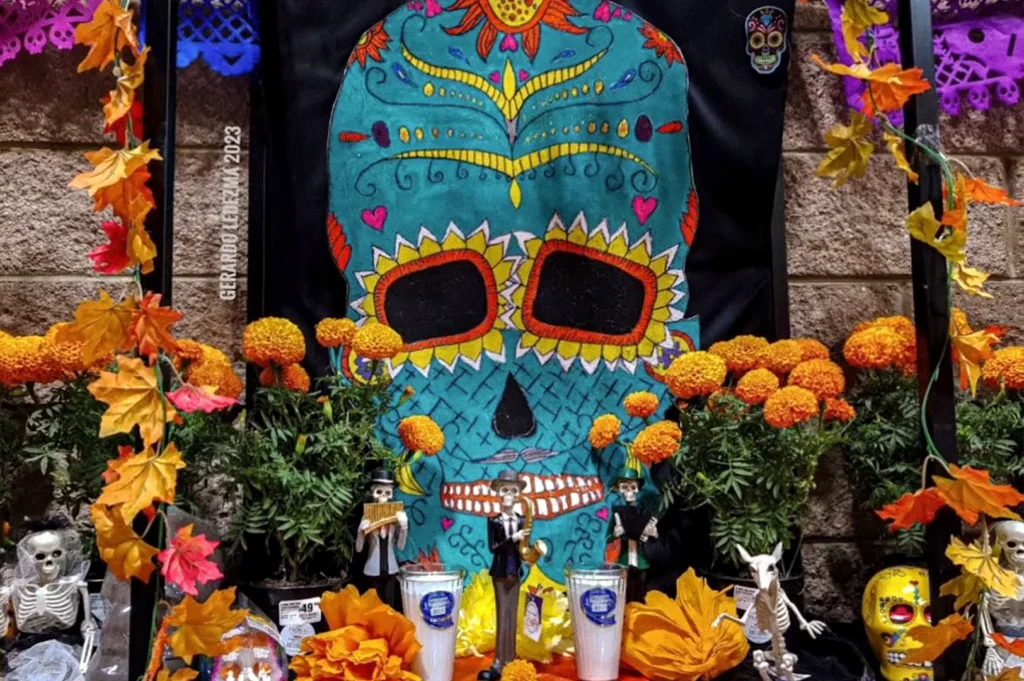Colorfully painted Day of the Dead skull display surrounded by marigolds, autumn leaves, miniature skeleton figures, and decorative skulls.
