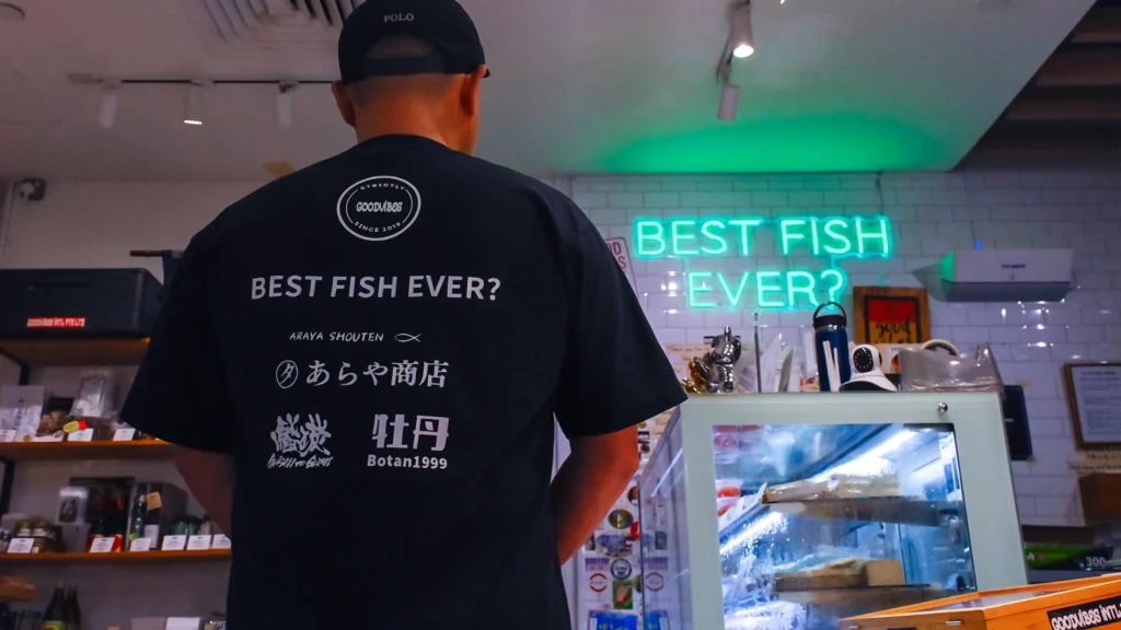 Araya Shouten staff member standing inside the Japanese fishmonger shop, with seafood displays and the “Best Fish Ever?” sign in the background.