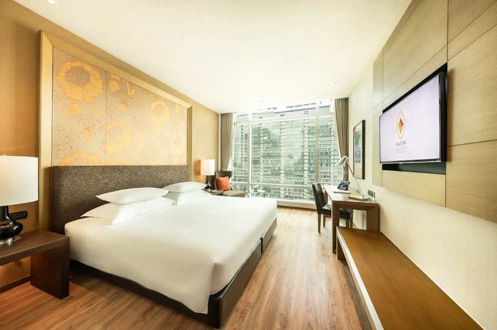 Modern Eastin hotel guest room with a large bed, wooden flooring, work desk, wall-mounted TV, and floor-to-ceiling window overlooking the city.