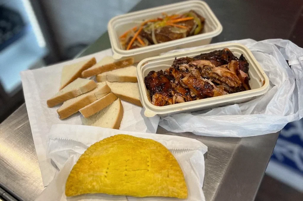 A takeaway spread featuring chopped roasted chicken, slices of white bread, a container of meat with vegetables, and a large golden-yellow pastry.