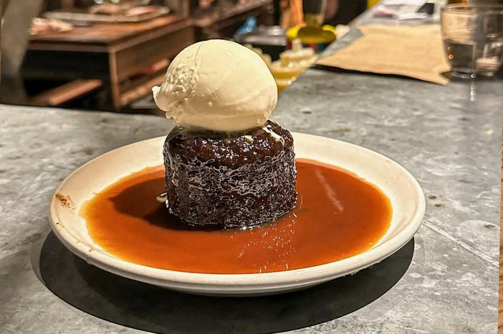 A rich chocolate fondant cake topped with a scoop of vanilla ice cream and surrounded by glossy caramel sauce on a white plate.